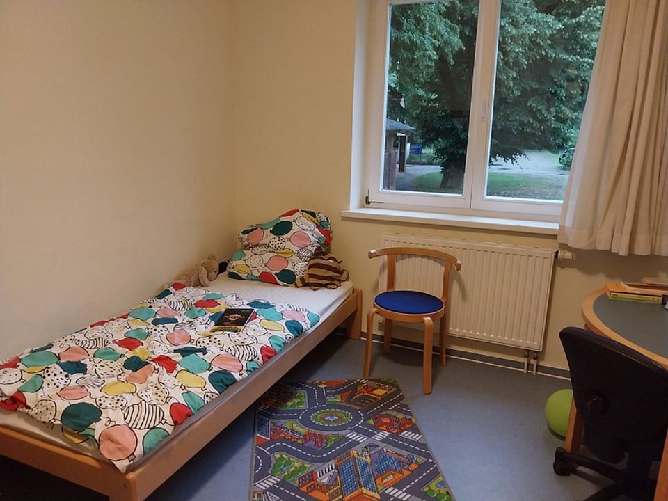 Bild zeigt einen Blick in ein Zimmer mit Bett, Tisch, Stuhl
