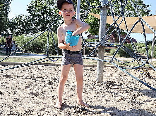 Bild zeigt einen Jungen der Spaß hat mit Wasser und Sand zu spielen