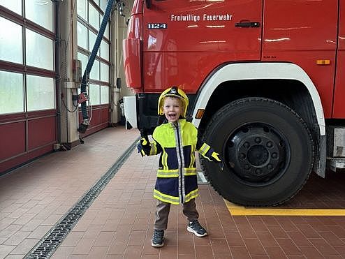 Bild zeigt einen kleinen Jungen in einer Jugendfeuerwehrkleidung vor einem großen Feuerwehrauto.