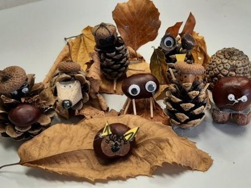 Bild zeigt ein Stillleben aus gebastelten Kastanien- und Eichel-Figuren, die mit trockenen Herbstblättern drapiert sind.