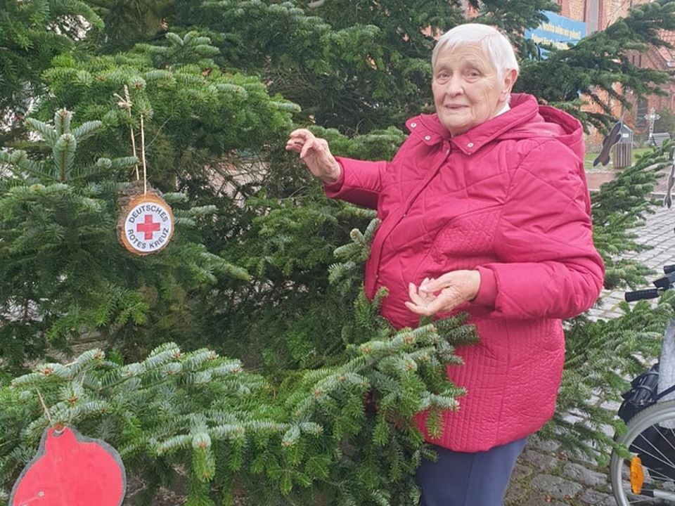 Bild zeigt eine Besucherin der Tagespflege bei aufhängen von Dekoration für den großen Weihnachtsbaum vor dem Krakower Rathaus