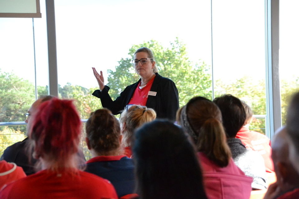 Cornelia Heidenreich, Bereichsleitung ambulante Pflege Bild zeigt Frau Heidenreich vor einer Glasfensterfront stehend und zu den Mitarbeitern sprechend.