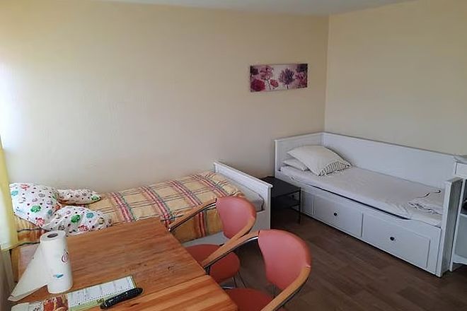 Bild zeigt einen Blick in ein Zimmer im Frauenschutzhaus, eingerichtet mit zwei Betten, eines davon als Tagessofa nutzbar, weiterhin Tisch und Stühle