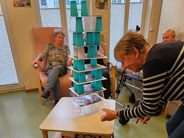 Bild zeigt eine Besucherin der Tagespflege bei einem Geschicklichkeitsspiel mit Einwegbechern und Platten auf denen die Becher aufgestapelt sind