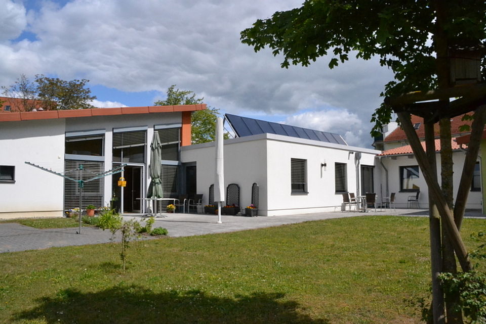Bild zeigt das Gebäude der Seniorenwohngemeinschaft mit Terrasse und weiteren Sitzmöglichkeiten im Außenbereich