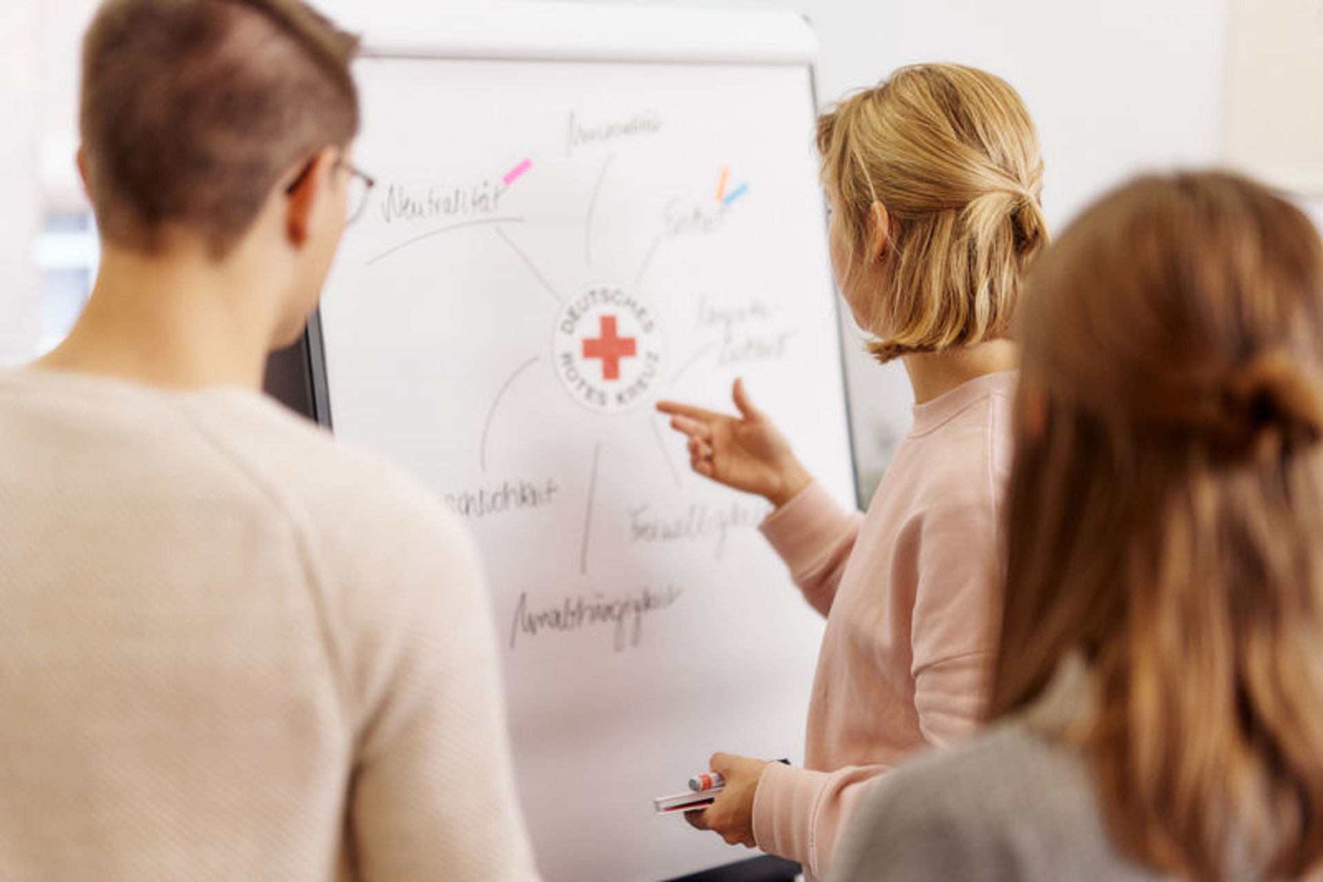 3 Personen stehen vor einem Flipchart und diskutieren über die auf dem Flipchart aufgeschriebenen Themen