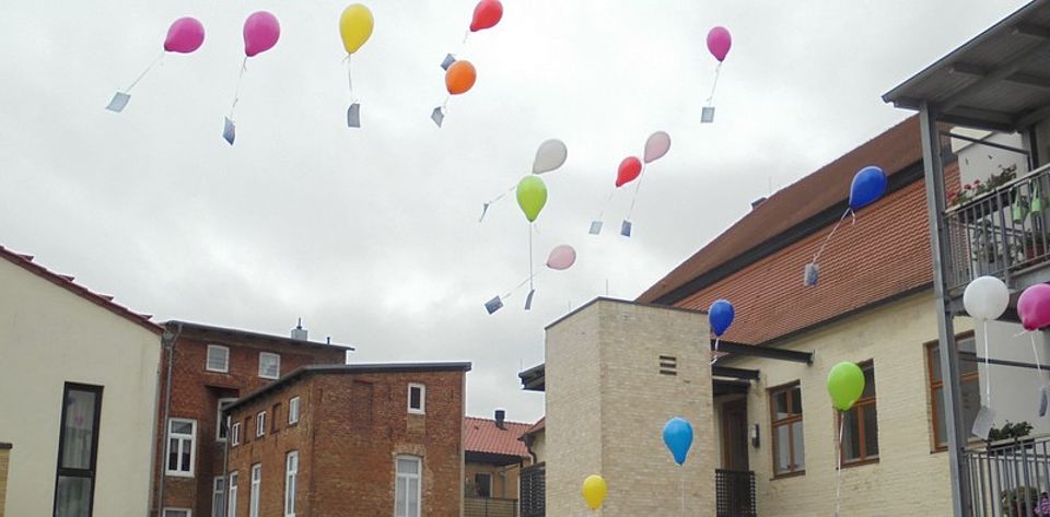 Bild zeigt aufsteigende Luftballons an denen Wunsch- und Grußkarten der Gäste der Tagespflege befestigt sind