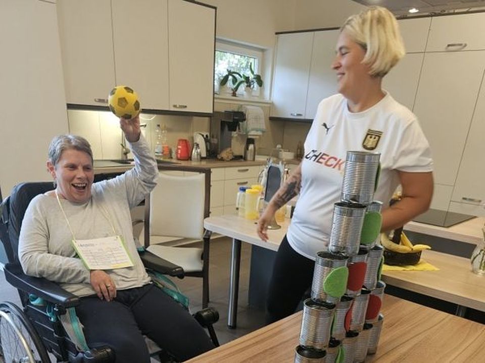 Bild zeigt ein Frau, Tagesgast in der Tagespflege, bei einer sportlichen Aktivität. Sie sitzt im Rollstuhl und macht Dosen werfen