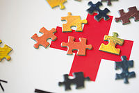 Bild zeigt im Hintergrund das Rote Kreuz darüber liegen bunte Puzzleteile