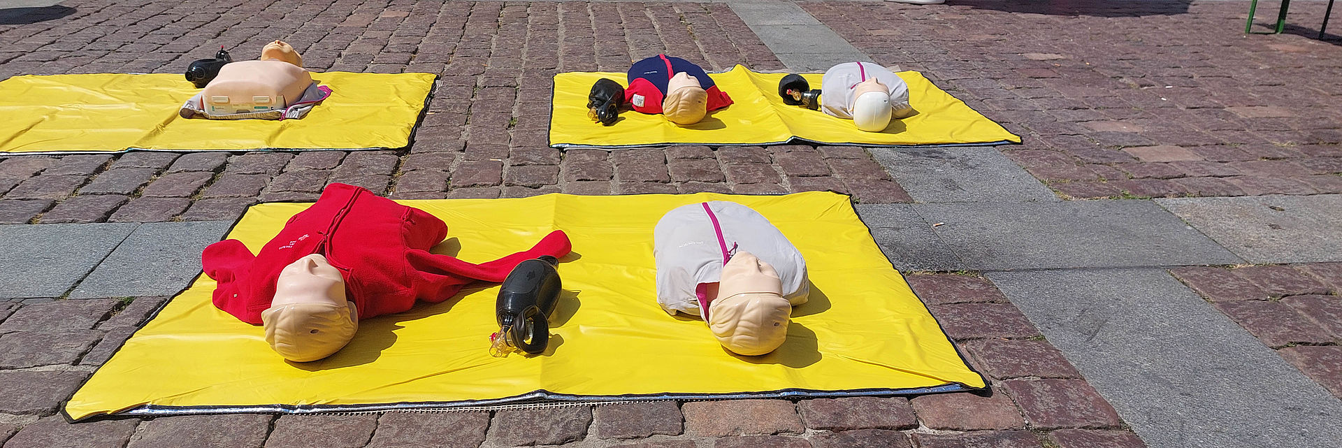 Bild zeigt Übungspuppen für Beatmung und Herzdruckmassage, welche auf dem Güstrower Marktplatz ausgelegt sind an denen Passanten üben können