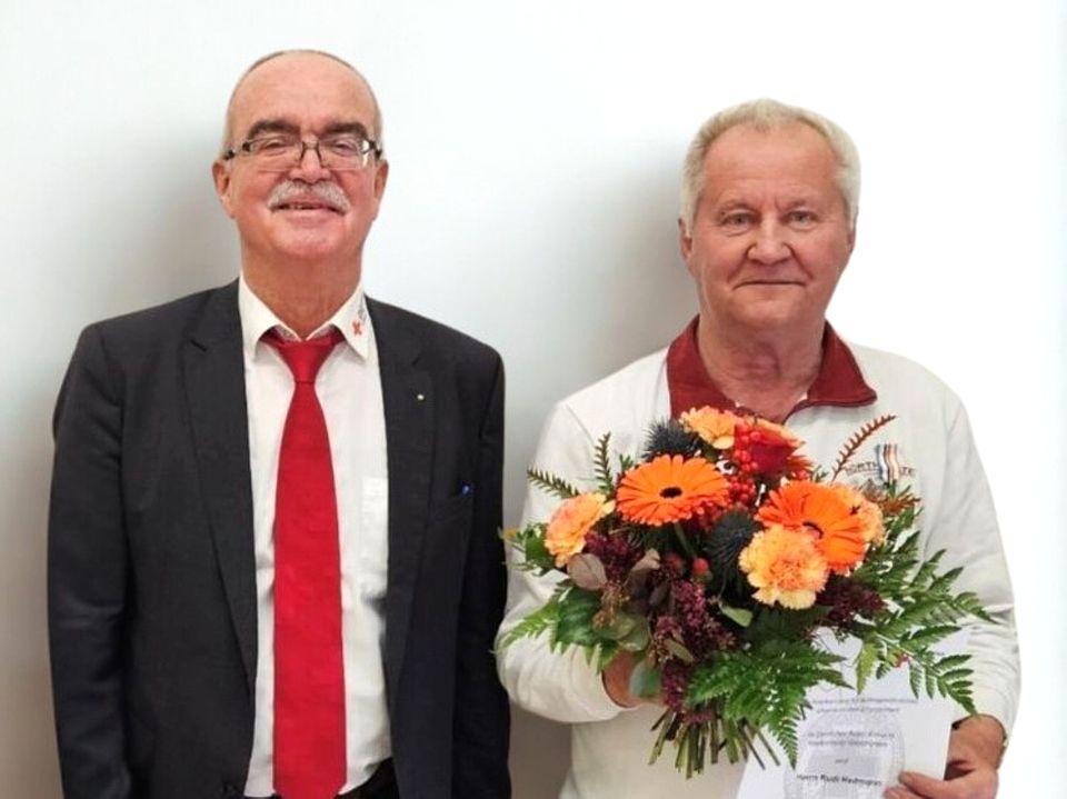 Werner Kuhn zeichnet Rudi Heitmann aus. Bild zeigt Werner Kuhn, Präsident des DRK Landesverband, und Rudi Heitmann nebeneinander stehen und in die Kamera blickend. Herr Heitmann hält einen schönen bunten Blumenstraß in den Händen, sowie die Urkunde der Auszeichnung.