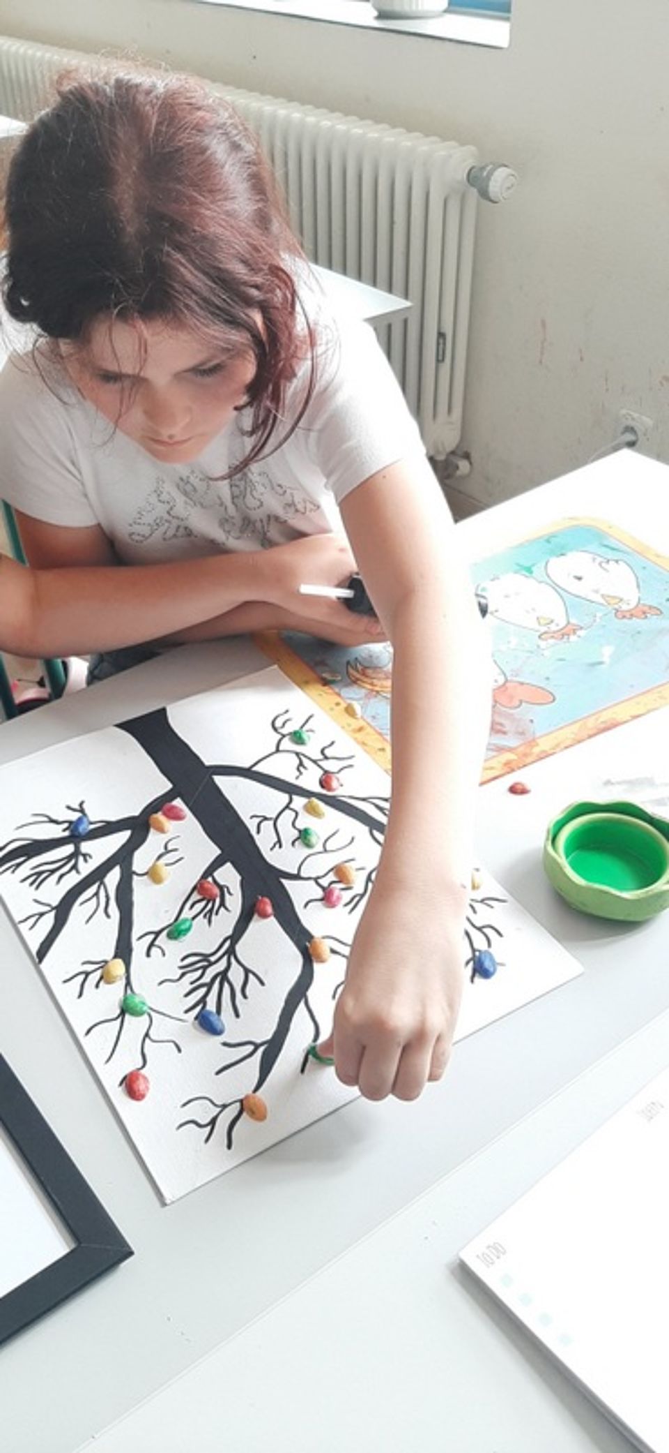 Bild zeigt ein Mädchen, welche auf ein Blatt Papier mit aufgemaltem Baum Pistazienschalen aufklebt