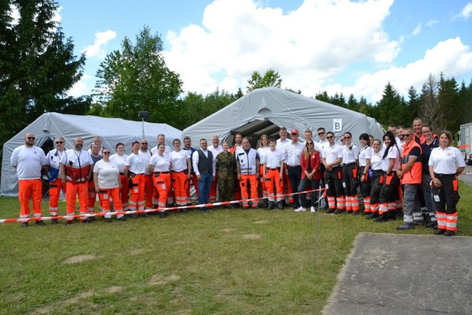 Bild zeigt eine Gruppenaufnahme aller am Absicherungseinsatz teilnehmenden DRK Einsatzkräfte. Die Gruppe von 38 Leuten steht im Halbkreis vor den Einsatzzelten des DRK