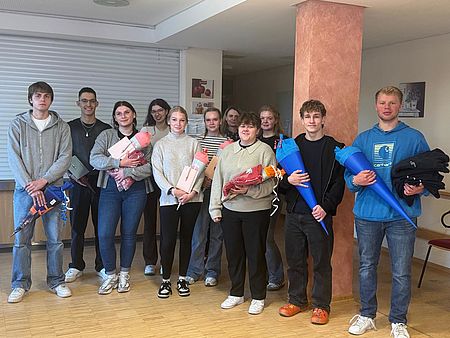 Bild zeigt 11 Auszubildende als Gruppe zusammenstehend für ein Gruppenfoto. Alle halten ihre "Schultüte", welche sie zum Start der Ausbildung geschenkt bekommen haben in den Händen.
