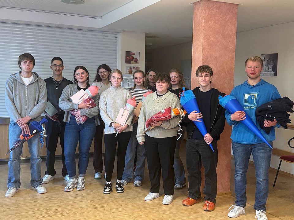 Bild zeigt 11 Auszubildende als Gruppe zusammenstehend für ein Gruppenfoto. Alle halten ihre "Schultüte", welche sie zum Start der Ausbildung geschenkt bekommen haben in den Händen.