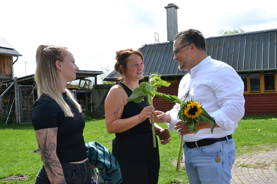 Bild 2 Bild zeigt die Übergabe einer Sonnenblume durch den Vorstandsvorsitzenden Alexander Plass an Frau Elena Fehlhaber, neben ihr steht Nele Bruchnow
