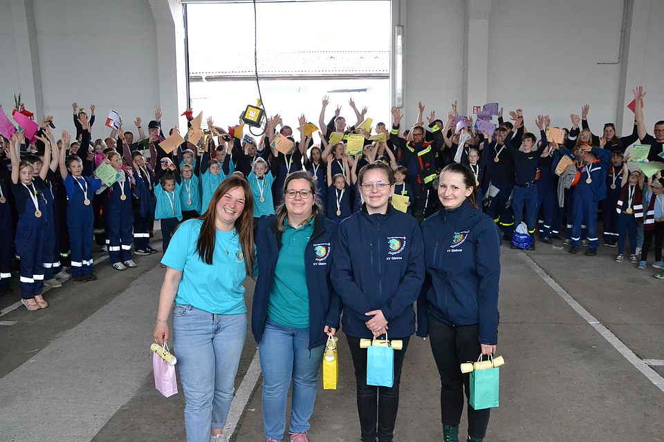 Bild zeigt die vier Hauptorganisatoren des Wettbewerbs. Im Hintergrund stehen alle Mannschaften im Karree und jubeln