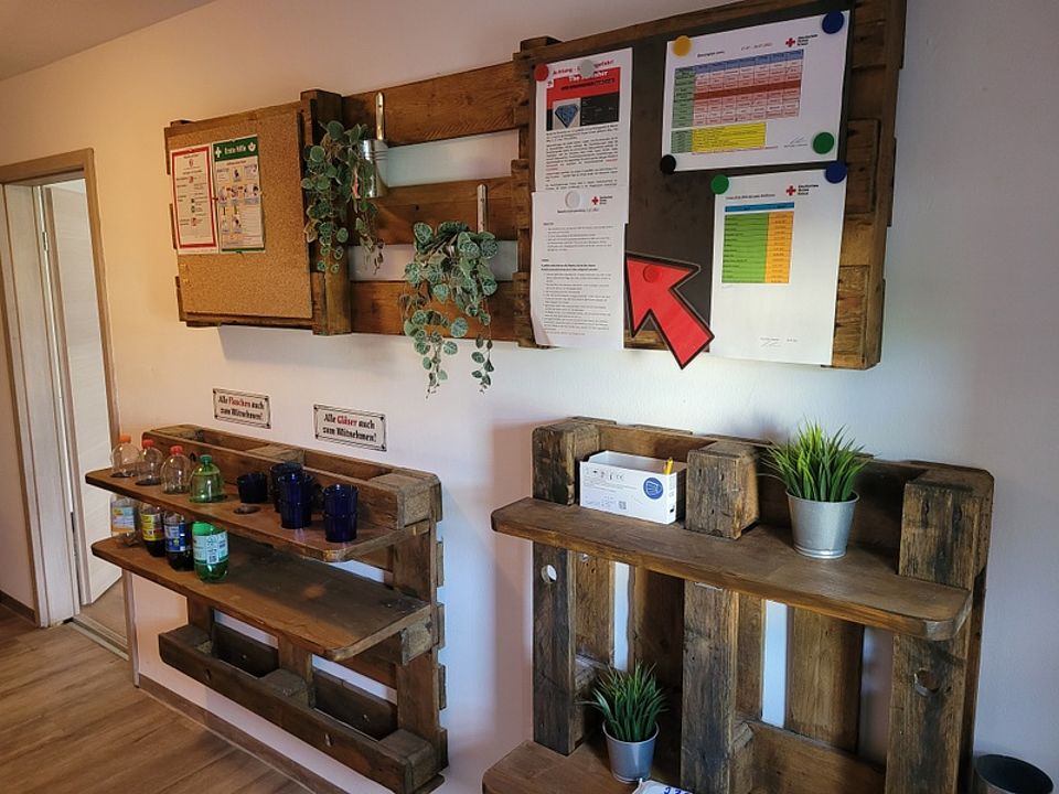 Bild zeigt eine Wandgestaltung aus EURO Paletten, welche als Regal, Getränkehalter und Infoboard dienen