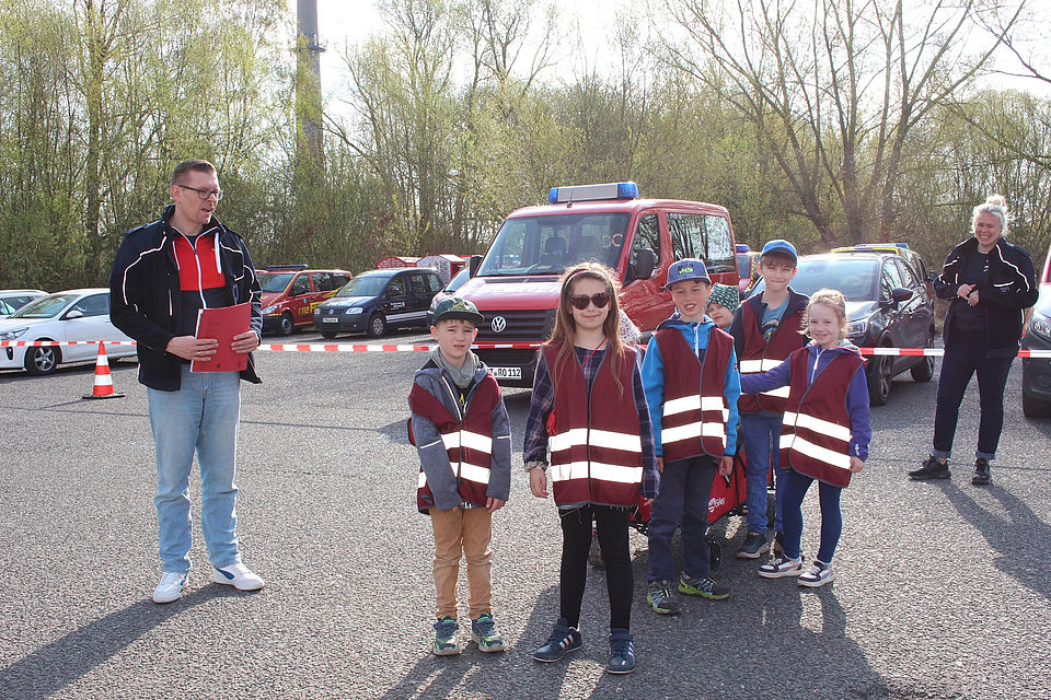 Bild zeigt eine Gruppe von Kindern (6 - 8 Jahre alt) die an der Startposition für den Wettkampf auf einem abgesperrten Parkplatz neben einem Schiedsrichter stehen und auf ihren Start warten.