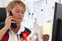 Bild zeigt eine Frau - Pfledienstleitung - bei einem Telefonat vor ihrem Computer