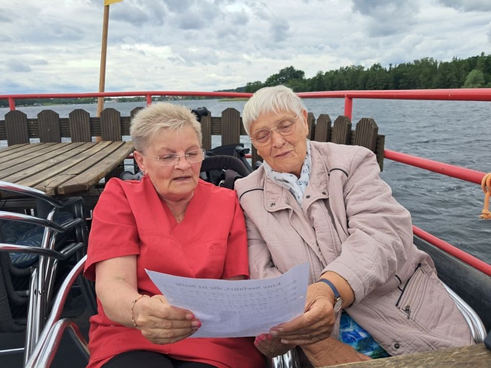 Bild zeigt zwei Besucherinnen der Tagespflege auf dem Schiff Seestern mit einem Liedblatt in der Hand fröhlich singend.