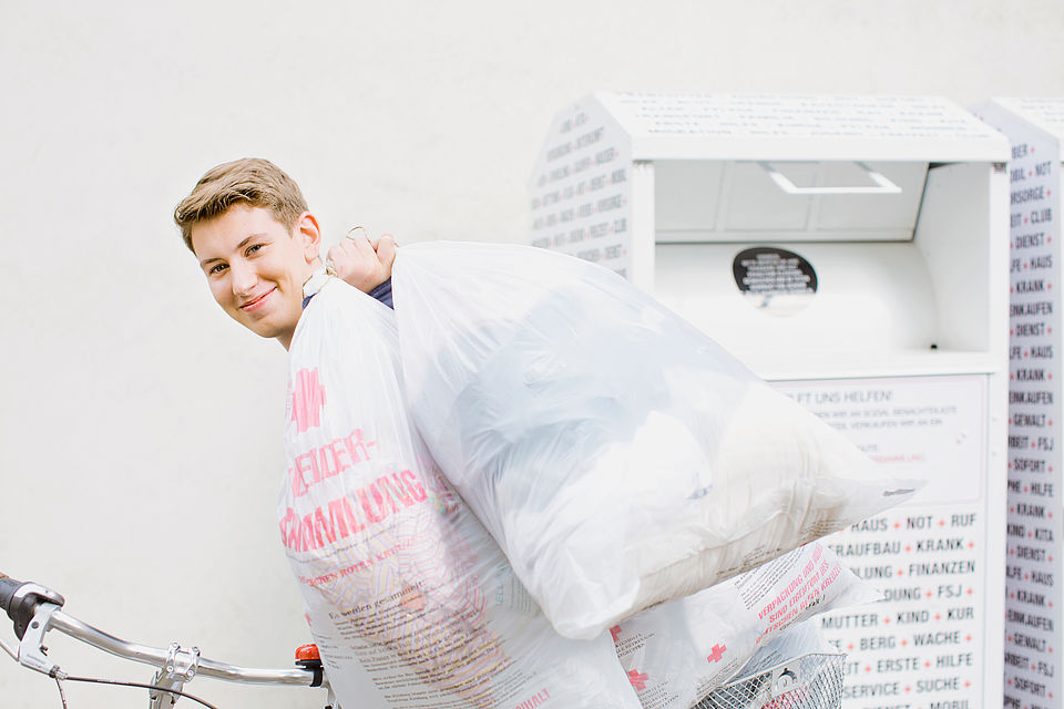 Bild zeigt einen jungen Mann, der mit mehreren Kleidersäcken vom Kleidercontainer weggeht