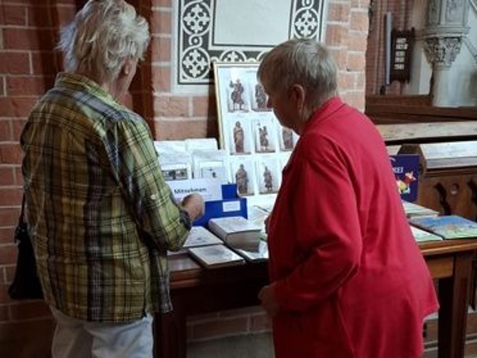 Bild zeigt zwei Frauen (Rückenansicht) vor einem Ausstellungstisch im Güstrower Dom. Auf dem Tisch sind Bücher und Karten zu sehen.