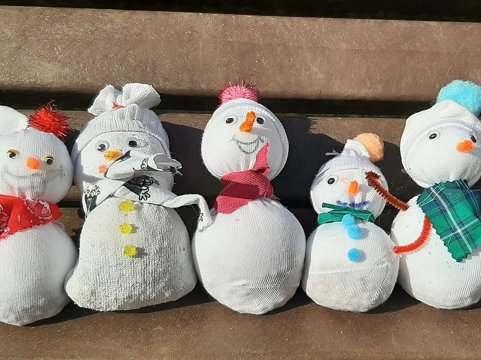 Bild zeigt eine Bank auf der 5 kleine, gehäkelte Schneemänner sitzen