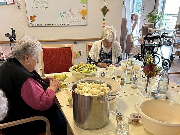 Bild zeigt mehrere Seniorinnen, welche Äpfel schälen und klein schneiden in Vorbereitung zum Kuchen backen