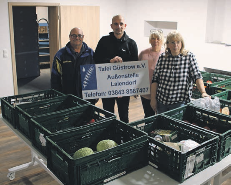 Bild zeigt die in der Bildunterschrift genannten 4 Personen von links nach rechts. Herr Marzahn hält das Schild in den Händen . Auf den Tischen vor den Personen stehen grüne Kisten mit Lebensmitteln die zur Verteilung vorgesehen sind.