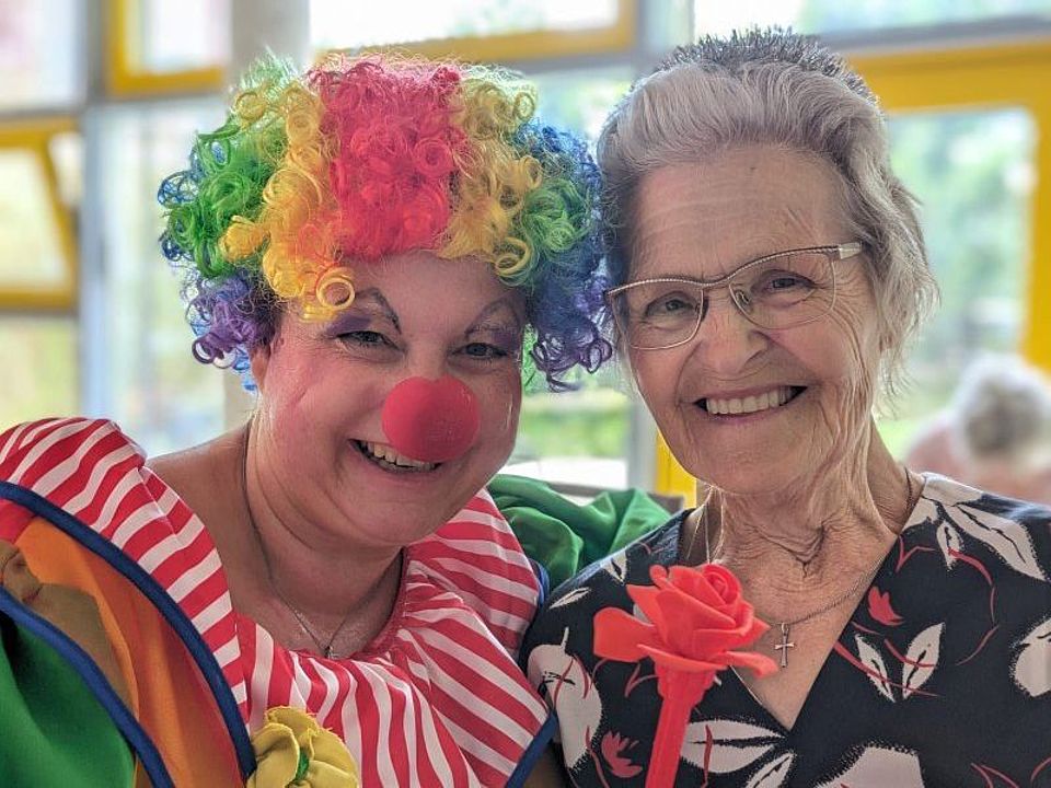 Bild zeigt eine als Clown verkleidete Mitarbeiterin, die mit einem Tagesgast vor der Kamera posiert