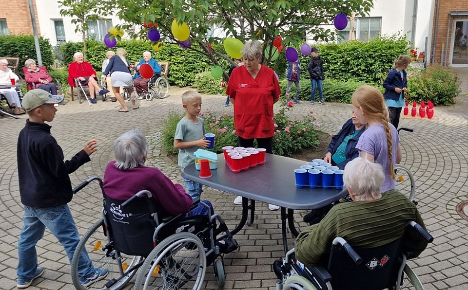 Bild zeigt einige Kinder und Senioren im Rollstuhl bei einem Ping-Pong-Becher Spiel an einem Tisch der im Freien aufgestellt ist