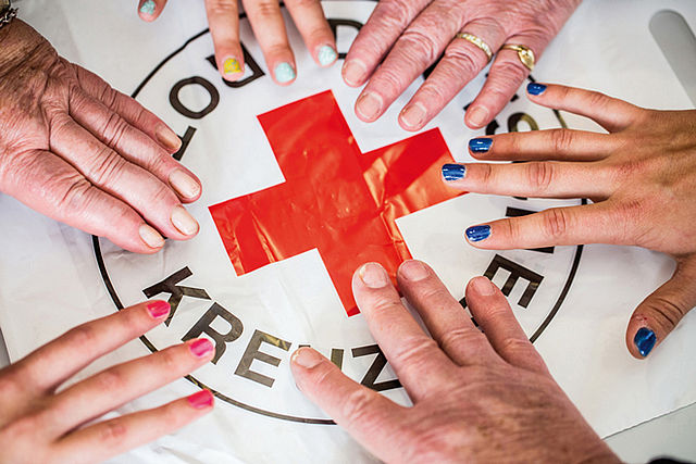 Bild zeigt ein DRK Emblem das von 6 Händen berührt wird