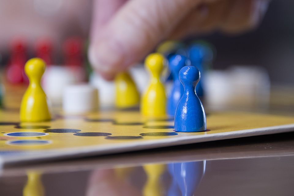 Bild zeigt in Nahaufnahme ein Mensch ärger dich nicht Spiel mit einer Hand, welche eine Figur greift