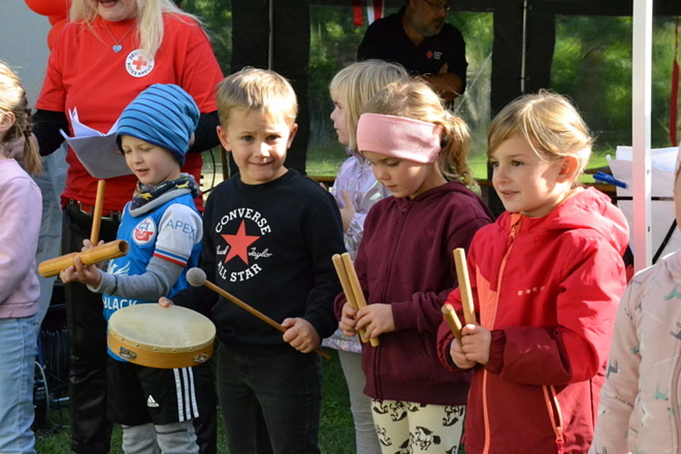 Bild zeigt mehrere Kinder der Kita mit Klanghölzern und Trommel bei der Darbietung eines Liedes. Die Kinder schauen sehr konzentriert auf ihre Instrumente.