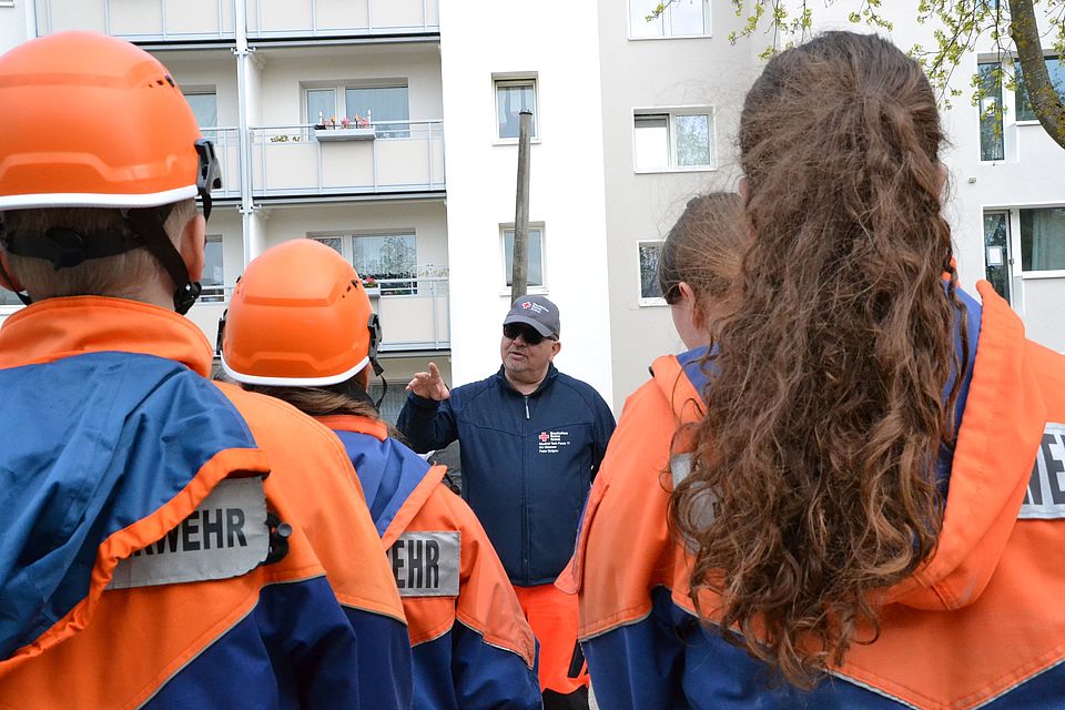 Bild zeigt eine Gruppe junger Feuerwehrkinder, welche mit dem Rücken zur Kamera stehen und dem Schiedsrichter Peter Dolgow aufmekrsam zuhören.
