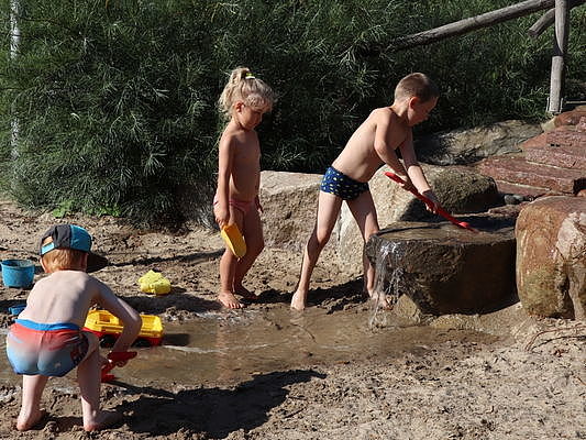 Bild zeigt mehrere Kinder in der großen Sandspielanlage mit Wasser matschen