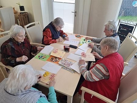 Bild zeigt 5 Tagesgäste am Tisch sitzend und die selbst gestalteten Grußkarten in Briefumschläge steckend
