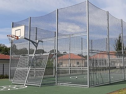 Bild zeigt einen Platz der mit Ballfangzäunen umgeben ist. Im Vordergrund ist ein Basketballkorb zusehen und im umzäunten Kasten ist das Kleinfußballfeld