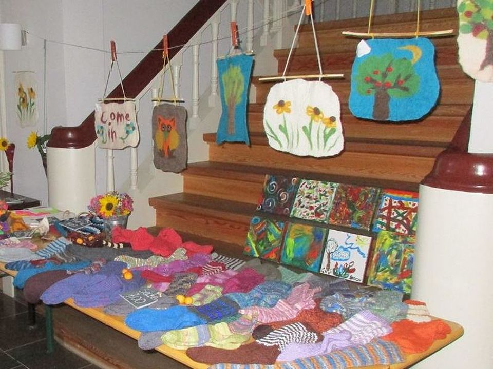 Bild zeigt eine Ausstellung von Gegenständen, welche die Besuchenden der Tagespflege selbst hergestellt haben. Unter anderem gestrickte Socken, Zeichnungen und aus Filz erstellte und mit verschiedenen Motiven verzierte Wandbehänge