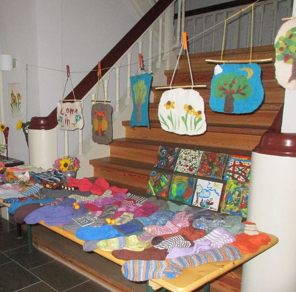Bild zeigt eine Ausstellung von Gegenständen, welche die Besuchenden der Tagespflege selbst hergestellt haben. Unter anderem gestrickte Socken, Zeichnungen und aus Filz erstellte und mit verschiedenen Motiven verzierte Wandbehänge