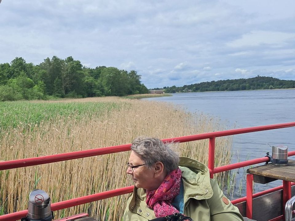 Bild zeigt in einem Halbporträt eine Besucherin der Tagespflege auf der Seestern, einem Ausflugsschiff für den Krakower See. Links im Bild ist ein Schilfgürtel zu sehen, rechts das Wasser des Krakower Sees.