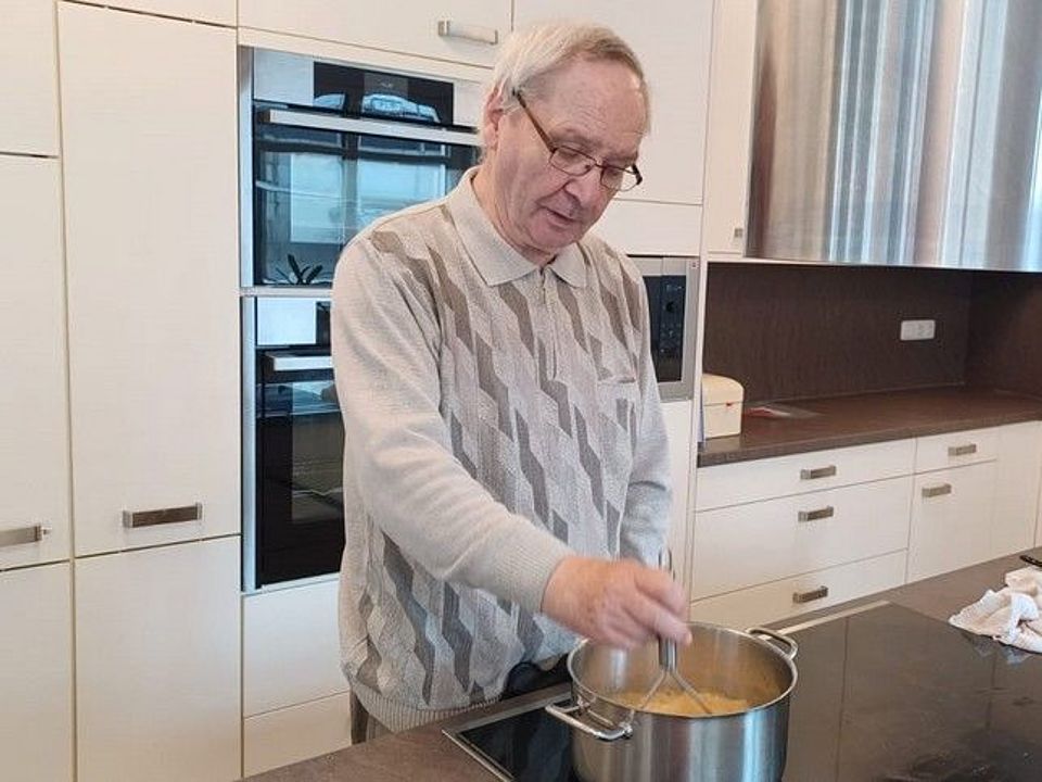 Bild zeigt Herrn Harald Wendel am Herd. Vor ihm steht ein Topf in dem die Apfelstücke eingekocht werden. Herr Wendel zerdrückt in dem Topf mit einem Kartoffelstampfer die Äpfel zu Mus.