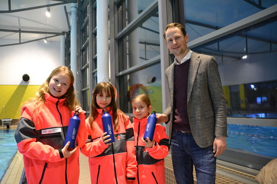 Juniorretter Bild 2 Bild zeigt die in der Bildunterschrift genannten drei Mädchen und Herrn Graßhoff. Die Mädchen halten dunkelblaue Trinkflaschen mit dem Logo der Stadtwerke in den Händen und schauen mit fröhlichen Gesichtern in die Kamera.