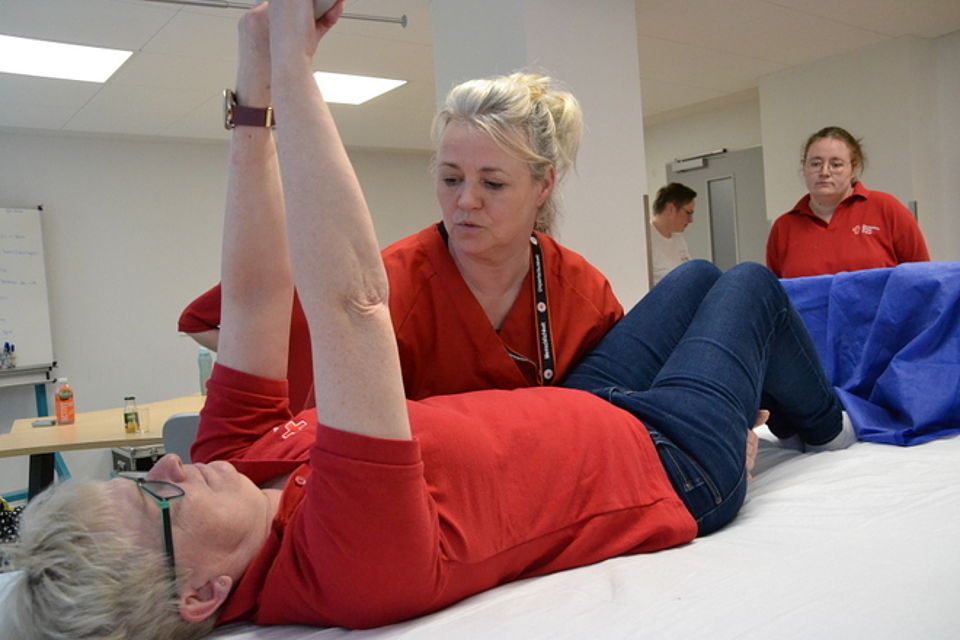 Bild zeigt zwei Auszubildende, eine liegt im Pflegebett und die zweite testet das umlagern mit und ohne Gleitmatte.