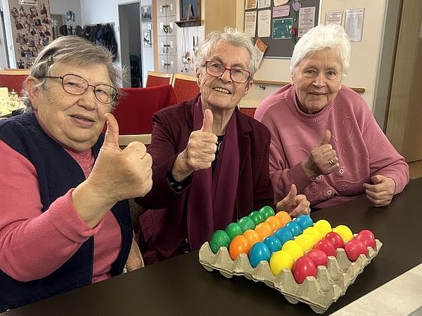 Bild zeigt drei Seniorinnen vor einer Palette gefärbten Ostereiern mit Daumen hoch