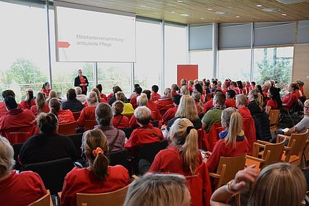 Bild zeigt einen großteil der Teilnehmenden der Mitarbeiterversammlung der ambulanten Pflege in Stuhlreihen sitzend und den Begrüßungsworten von Frau Cornelia Heidenreich zuhörend.