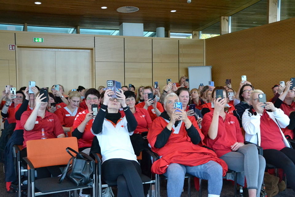 Online-Befragung Bild zeigt die Mitarbeitenden, wie sie mit ihrem Handy einen QR-Code von der Videowand abscannen um an einer online-Befragung teilzunehmen