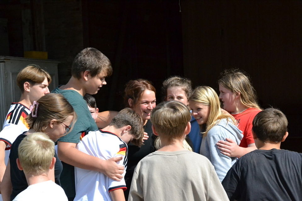 Bild 4 Bild zeigt einen großen Teil der Teilnehmenden wie sie sich voneinander verabschieden. In einigen Gesichtern sieht man ein Lachen in anderen etwas Wehmut. Alle zusammen umarmen sich