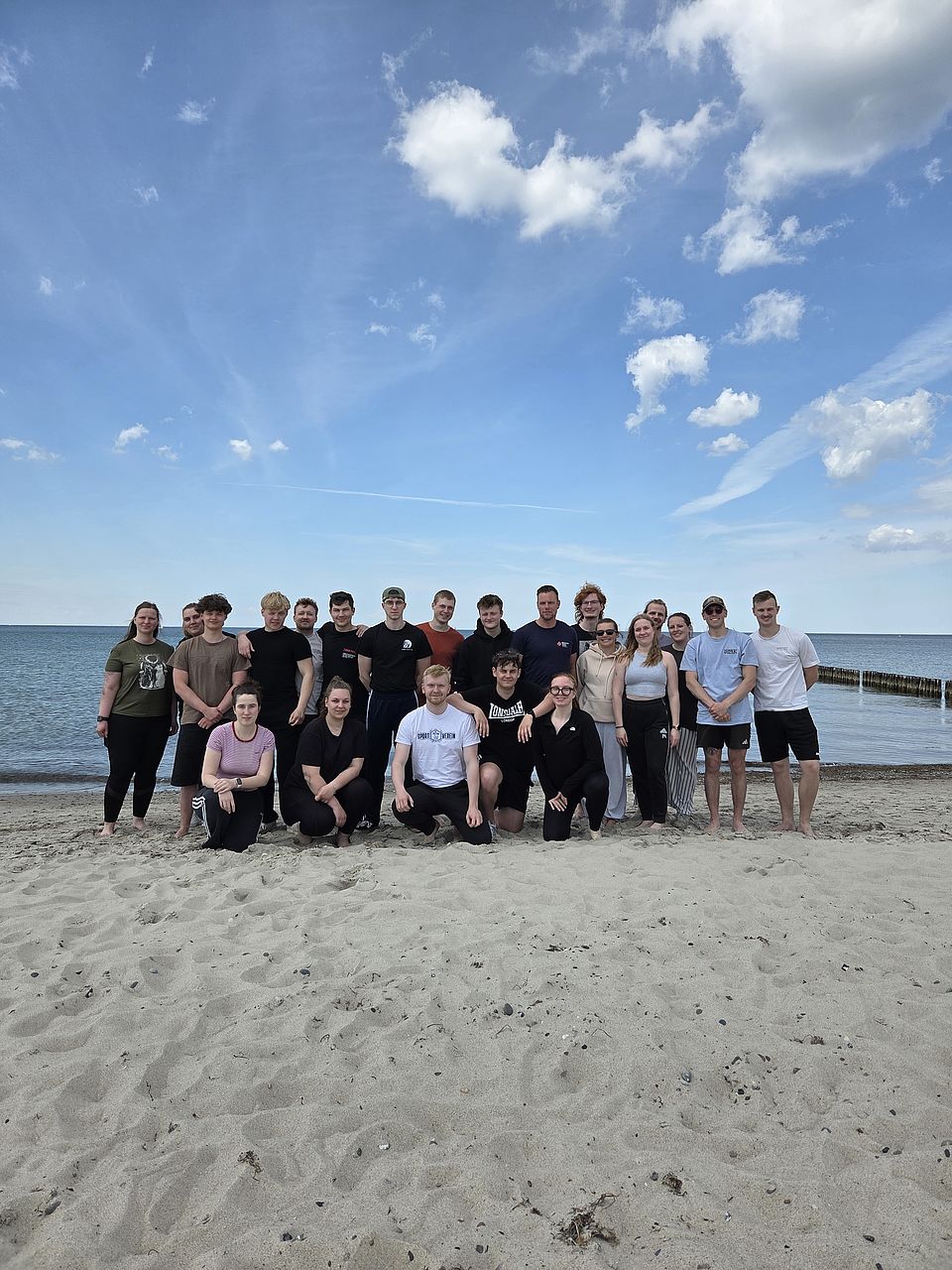 Bild zeigt eine Gruppe von 22 Personen, die sich am Strand der Ostsee zu einem Gruppenbild aufgestellt haben.